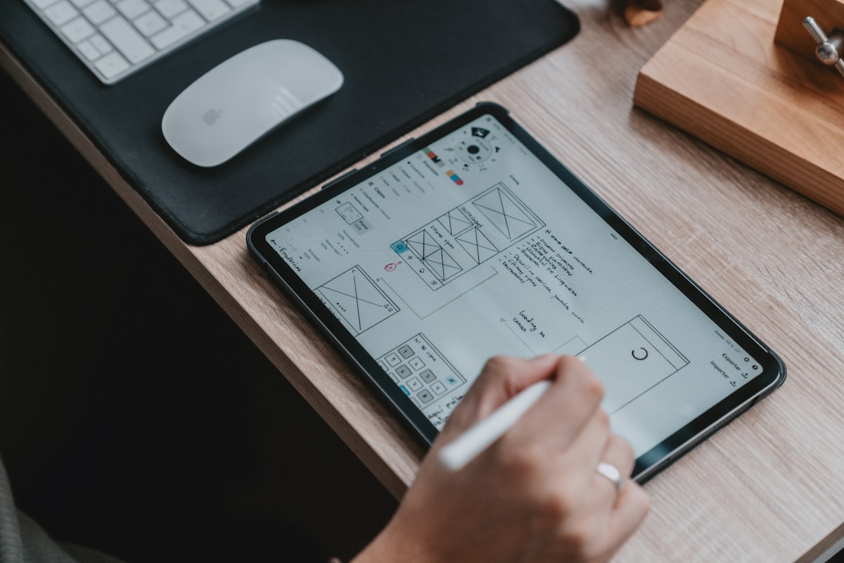 Freelance UX UI designer working on a Figma wireframe at a modern desk setup with laptop and tablet